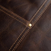Close-up of dark brown leather with diagonal stitching and a small brass rivet.