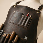 Close-up of textured brown leather apron chest showing utility pocket, pencil sleeves, stitched edges, metal rivets and brass-tone rings.