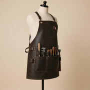 Side front view of brown leather woodworking apron holding chisels, measuring tools, ruler and hammer in multiple utility pockets and loops.