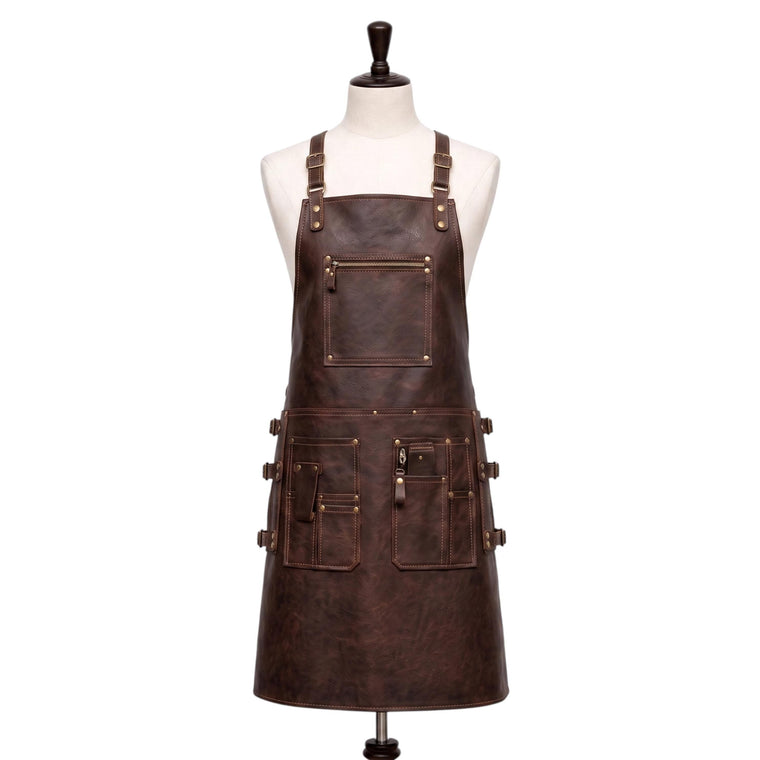 "Front view of a full-length dark brown leather apron displayed on a fabric mannequin, featuring adjustable neck straps with brass buckles, a zippered chest pocket, and multiple front pockets on the waist section with buckle straps and brass rivets, photographed against a plain white background."