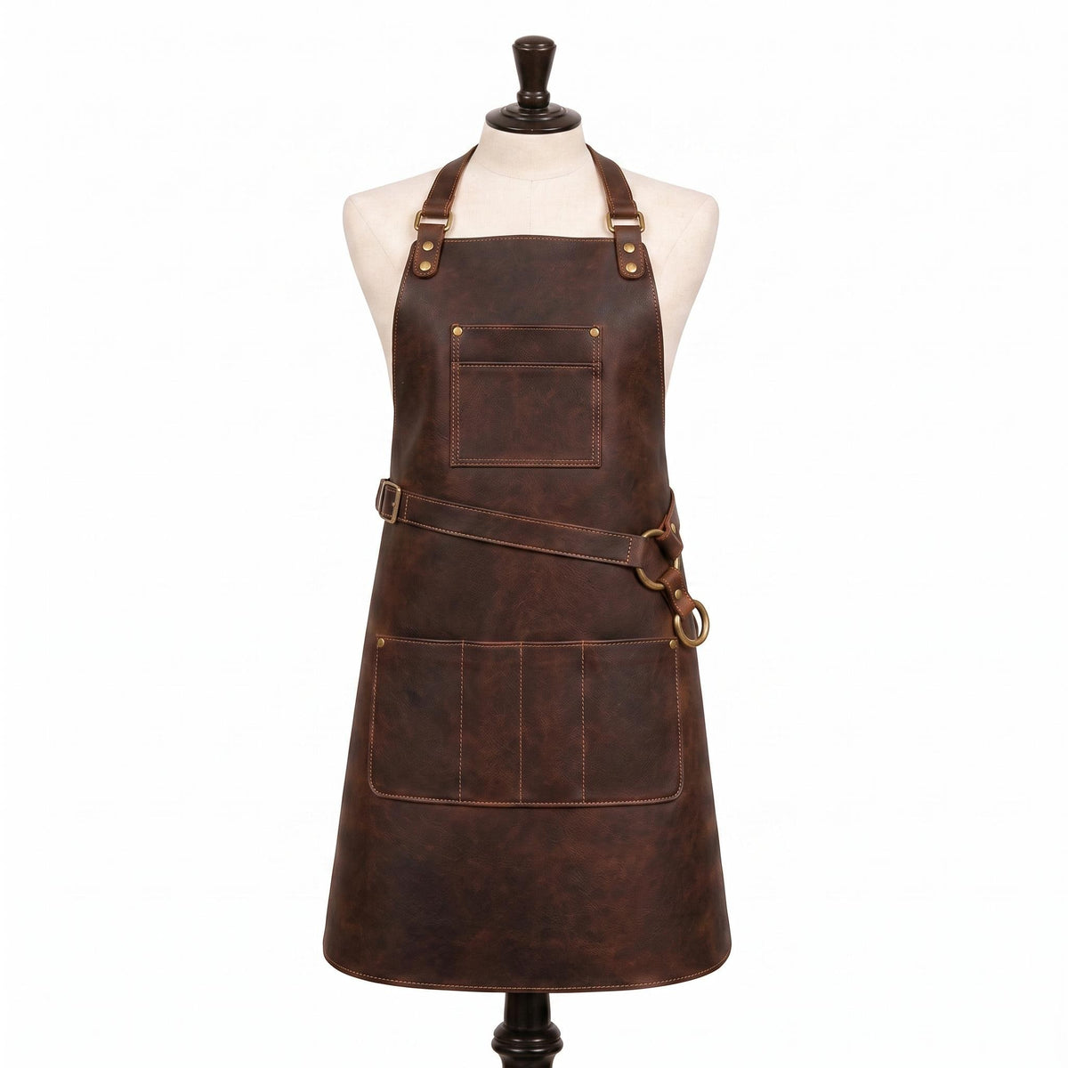 "Dark brown leather apron on a cream-colored mannequin torso, featuring an adjustable neck strap with brass buckle and rivets, a cross-back waist strap with a brass D-ring, a single chest pocket, and a wide pocket panel with multiple compartments at the front lower section, set against a plain white background.