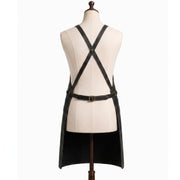 "Back view of black leather apron with crossback straps and adjustable brass buckle belt on a mannequin."