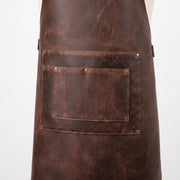 "Close-up of the leather apron's front pocket with rivets and stitched compartments."