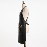 "Side profile of black leather apron with crossback straps and pockets full of paintbrushes."