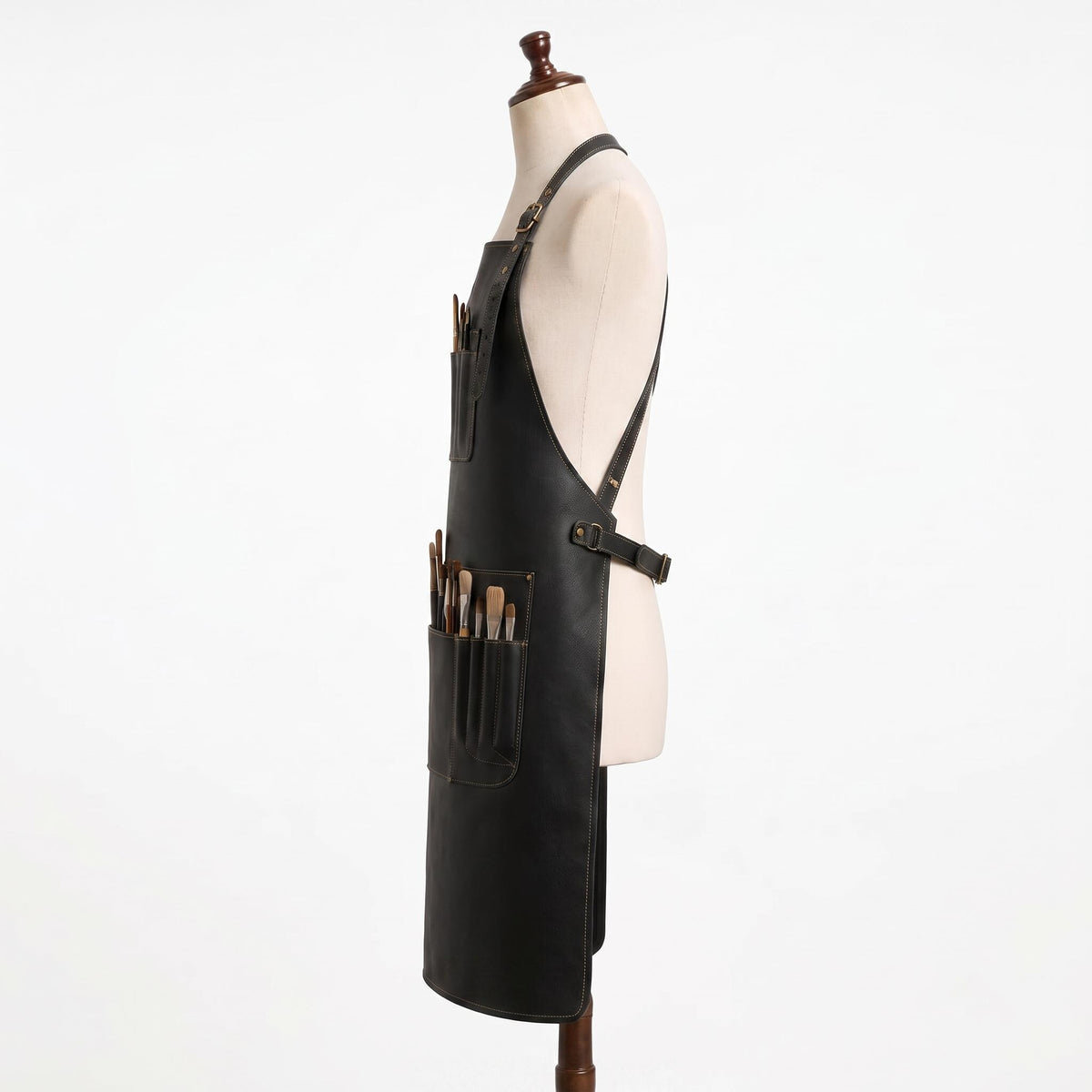 "Side profile of black leather apron with crossback straps and pockets full of paintbrushes."