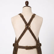 "Close-up of distressed brown leather apron's crisscross X-back straps with brass buckles, brass O-ring, and adjustable waist belt, shown on a mannequin torso."