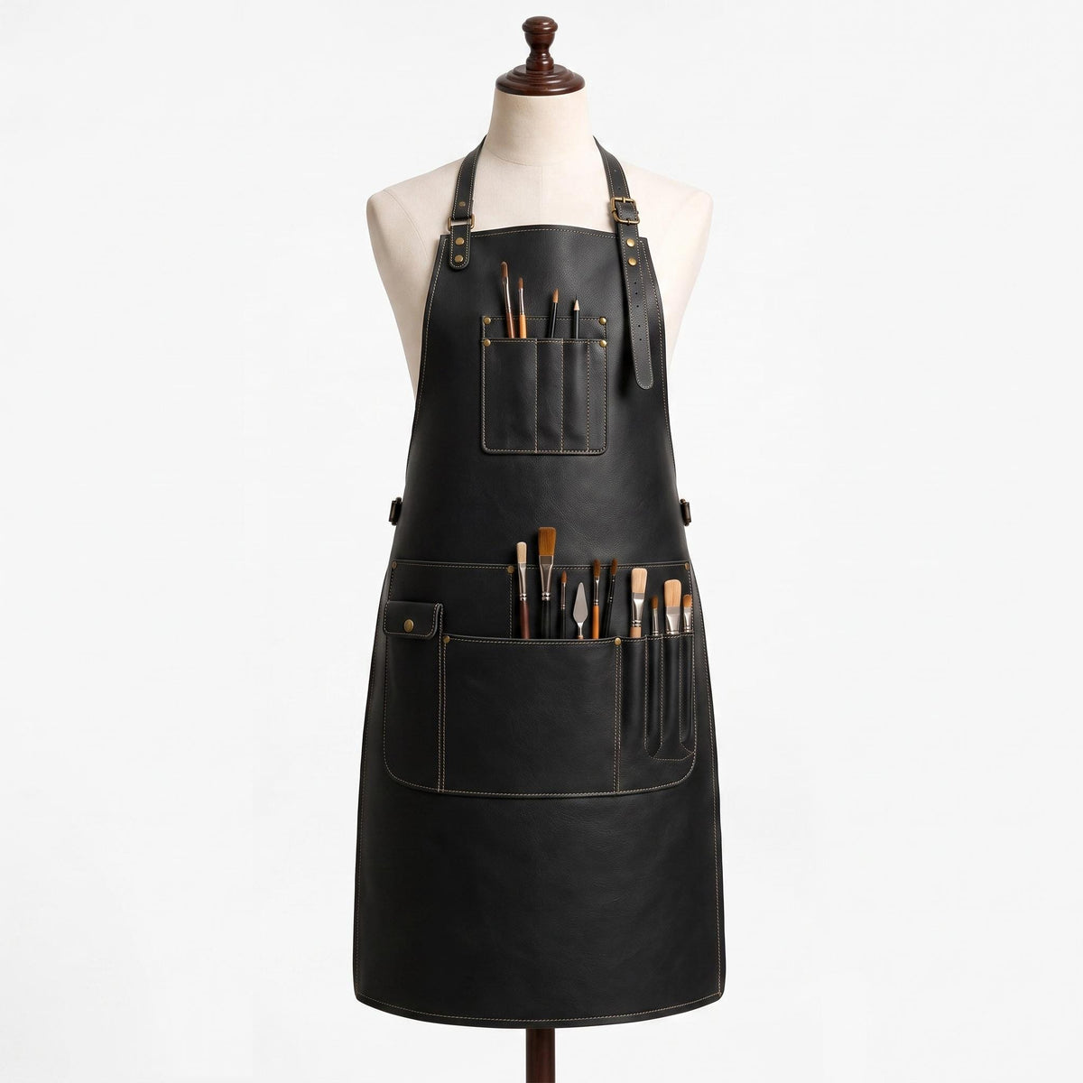 "Black leather artist's apron with multiple pockets holding paintbrushes and a palette knife, displayed on a mannequin against white background."