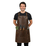 "Man wearing distressed brown leather gardening apron over a black t-shirt, with pockets holding a trowel, hand fork, pruning shears, and gardening gloves."