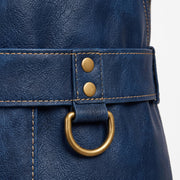 "Close-up of navy blue leather apron's waist belt, showing an adjustable strap with brass rivets, contrast stitching, and a brass D-ring attachment hanging below the belt."