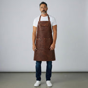 Man wearing brown leather apron with chest pocket and lower tool pockets over t-shirt and jeans
