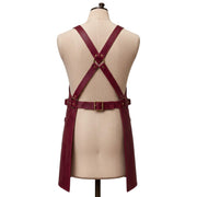 "Back view of a burgundy leather apron with crossback straps, a brass D-ring, and an adjustable waist buckle."