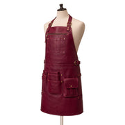 "Side-angle view of a burgundy leather apron with brass buckles, a zippered chest pocket, and multiple tool pockets on the front."