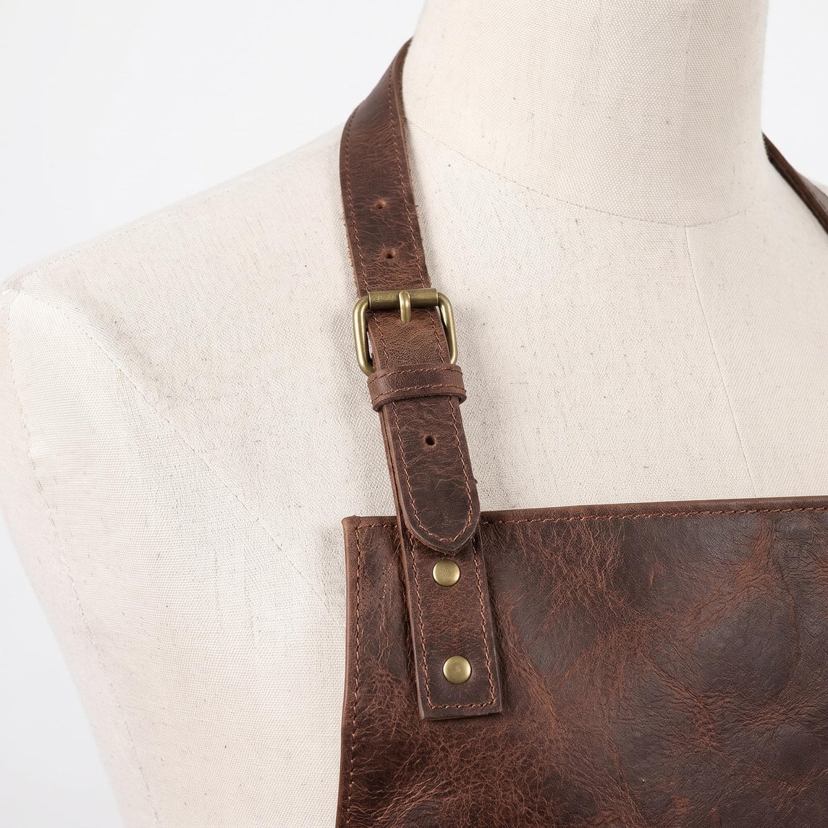 "Close-up of the leather apron's shoulder strap buckle and rivets."