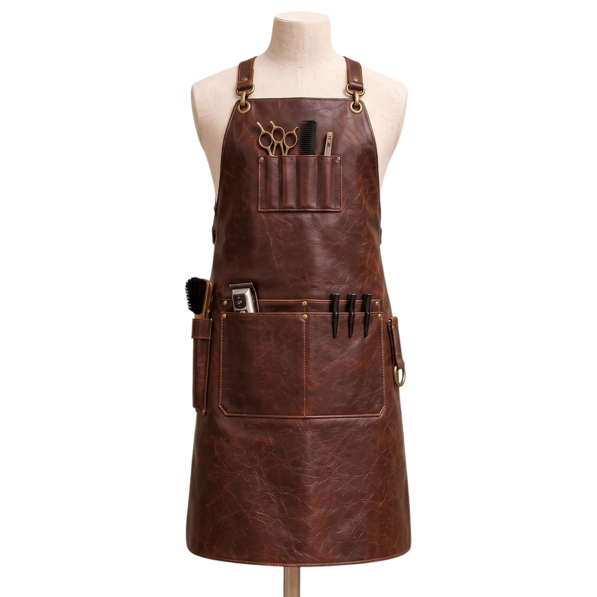 "Distressed brown leather barber apron with tool pockets holding scissors, comb, clippers, and brush, styled on a mannequin."