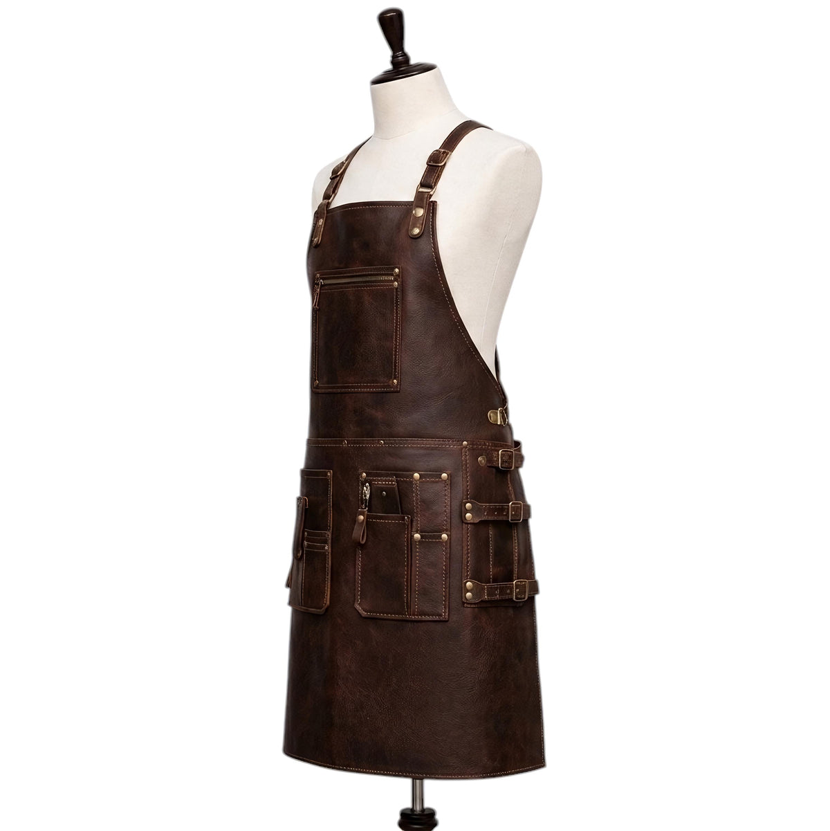 "Three-quarter side view of a dark brown leather work apron displayed on a fabric mannequin, showing adjustable shoulder straps with brass buckles, a zippered chest pocket, and multiple front tool pockets with buckle straps and brass rivets along the waist section, photographed against a plain white background."