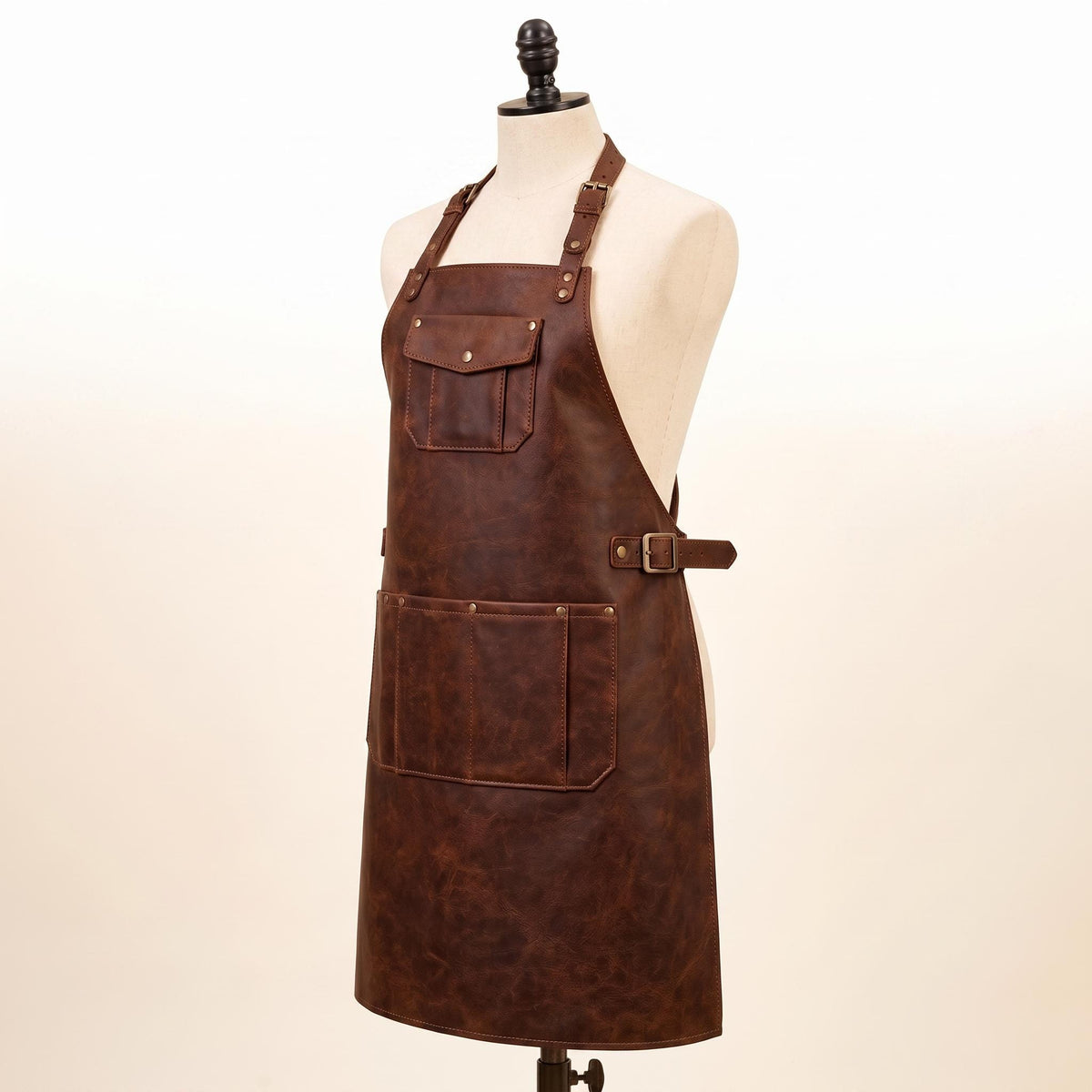 Side view of brown full-grain leather apron with adjustable buckle straps, front chest pocket, and large lower tool pocket, displayed on mannequin