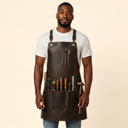 Dark brown leather work apron worn by a craftsman, featuring adjustable shoulder straps, multiple tool pockets and leather tool loops