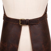 "Close-up back view of a dark brown leather apron's waist belt on a cream mannequin, showing a brass buckle closure with adjustable holes and contrast tan stitching, and the lower panel split into two hanging straps."