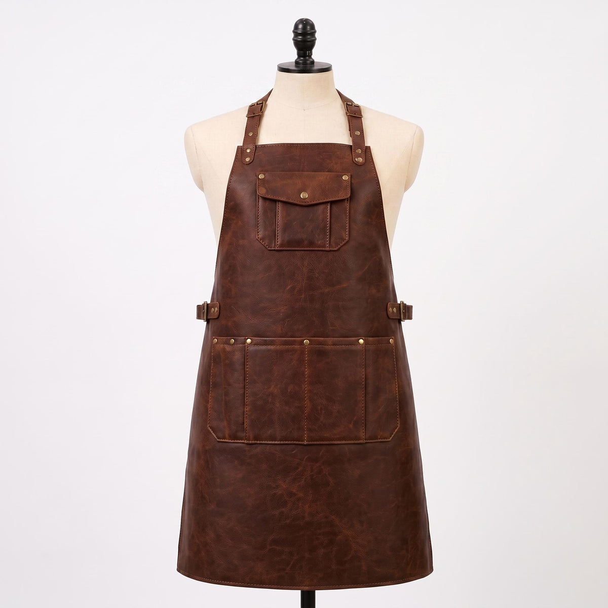 Brown leather BBQ apron with adjustable straps, waist belt, brass hardware and multiple utility pockets on mannequin.