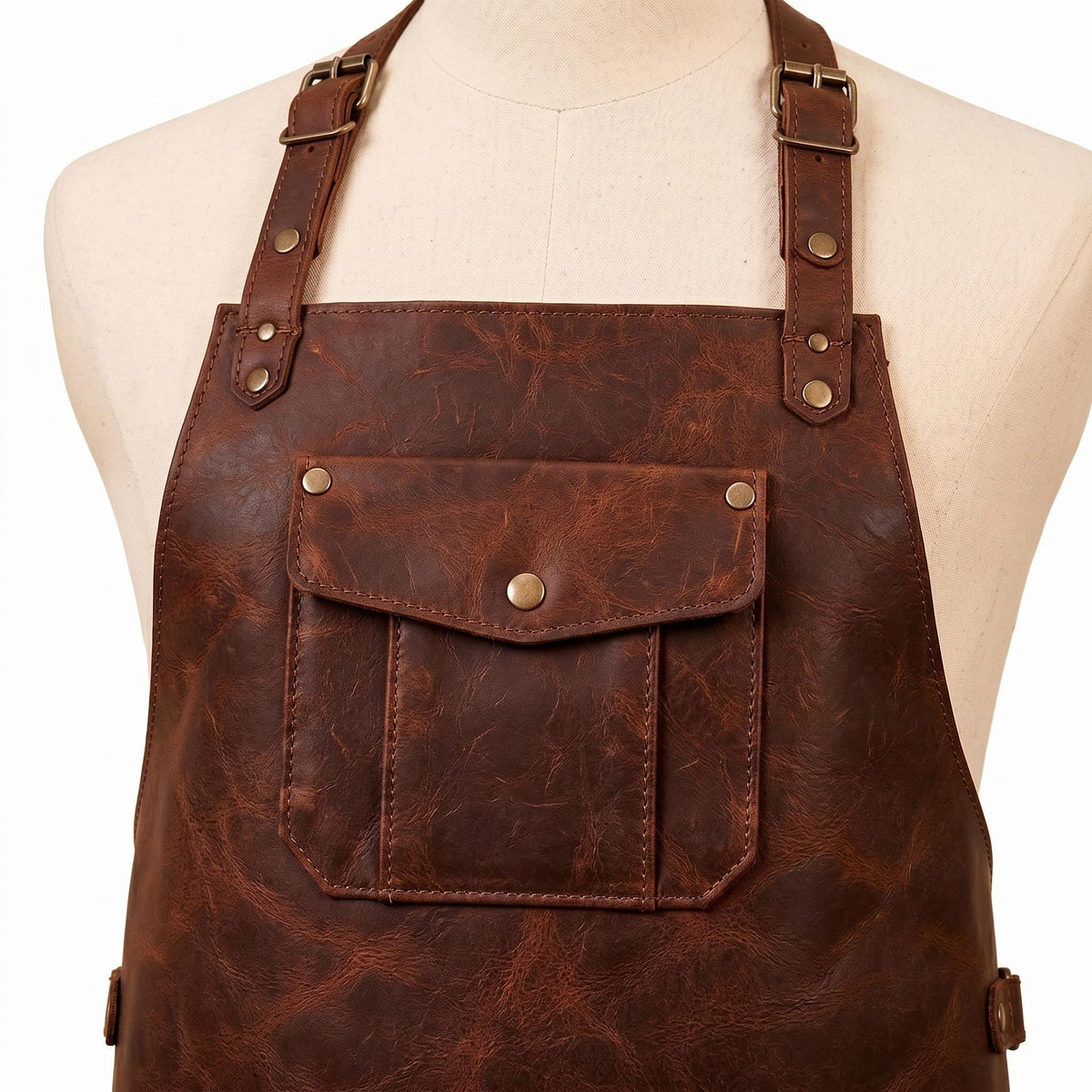 Close-up of leather apron chest pocket with brass snap button and adjustable neck strap buckles on mannequin