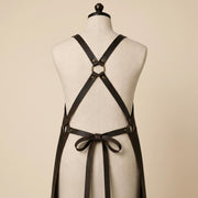 Back view of brown leather work apron showing adjustable cross-back shoulder straps, central metal ring and leather waist tie.