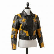"Angled view of a black leather biker jacket with yellow and gray star graphic panels, asymmetric front zipper, zip pockets, and belted waist, displayed on a mannequin against a white background."