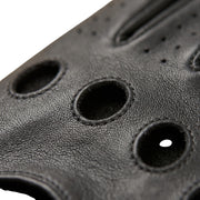 "Extreme close-up of the knuckle area on a black leather driving glove, showing large stitched ventilation holes, leather grain texture, and finger perforations."