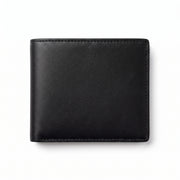 Front view product shot of a black leather bifold wallet, closed, lying flat with rounded corners, visible hand-stitched edges in matching black thread along the border, smooth grained leather surface, photographed against a plain white background with a soft shadow beneath."