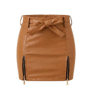 "Tan brown faux leather mini skirt with a tie-front bow belt and dual gold-tone front zippers, laid flat against a white background."