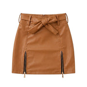 "Brown faux leather mini skirt with front tie bow belt, twin gold zipper details at hem, and back zip closure – women's fashion product photo on white background."