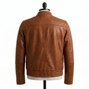 "Back view of a tan brown leather bomber jacket with ribbed collar and quilted elbow panels, displayed on a mannequin against a white background."