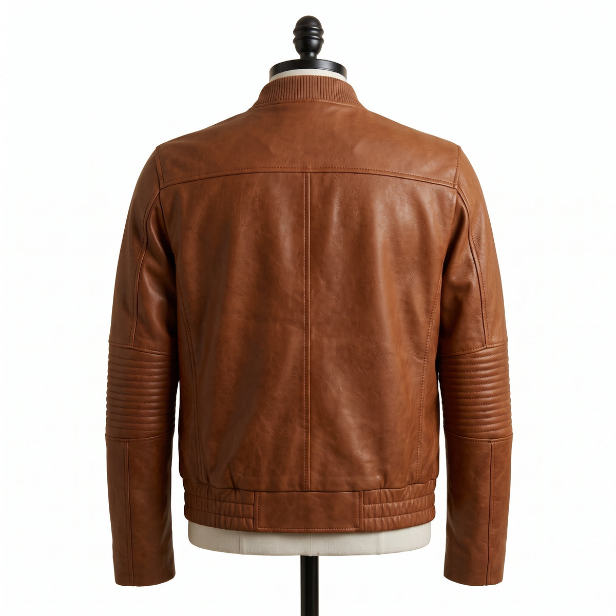 "Back view of a tan brown leather bomber jacket with ribbed collar and quilted elbow panels, displayed on a mannequin against a white background."