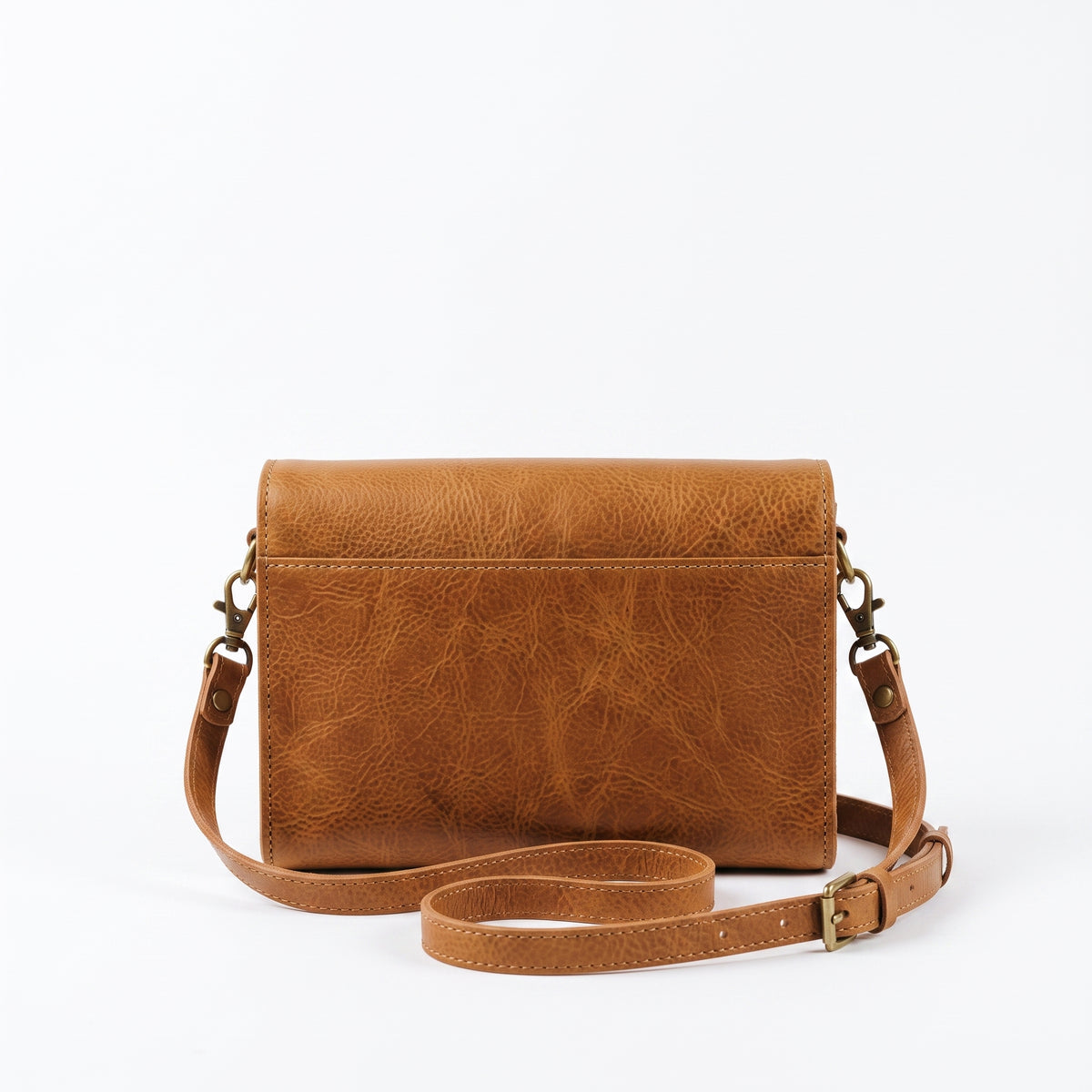 "Back panel view of a tan leather crossbody bag showing smooth leather, brass swivel hooks, and the adjustable strap with a buckle against a light background."