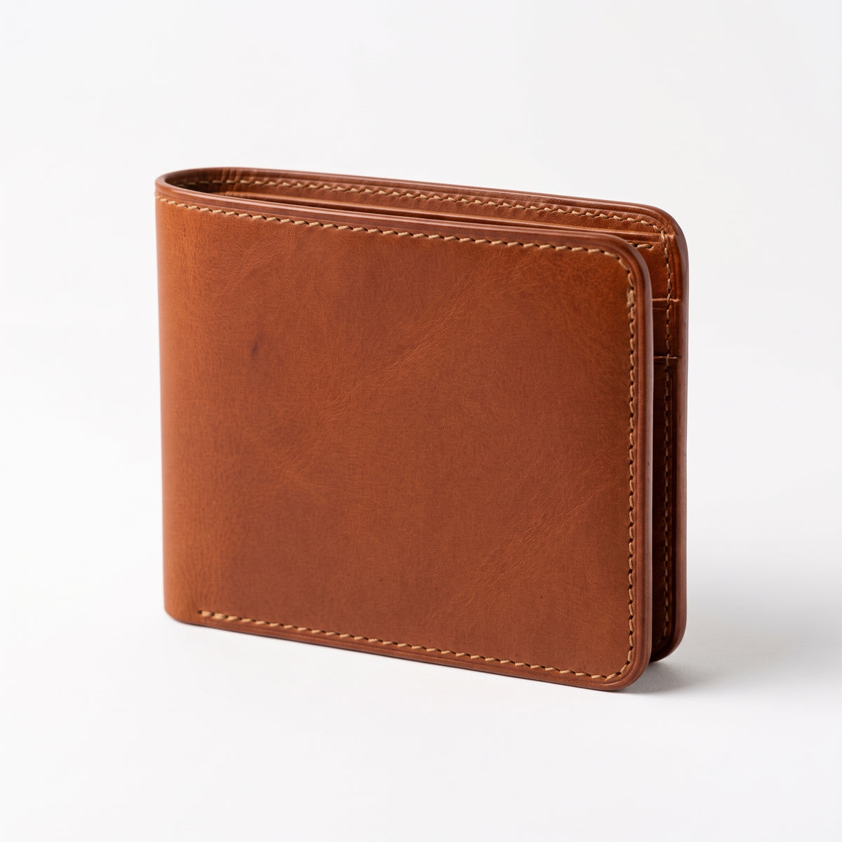 "Brown tan leather bifold wallet standing upright at a three-quarter angle on a light gray surface, showing rich natural leather grain with visible tonal variations, contrasting cream/tan stitching along the edges, and a slightly fanned interior spine, photographed with soft studio lighting and subtle shadow."