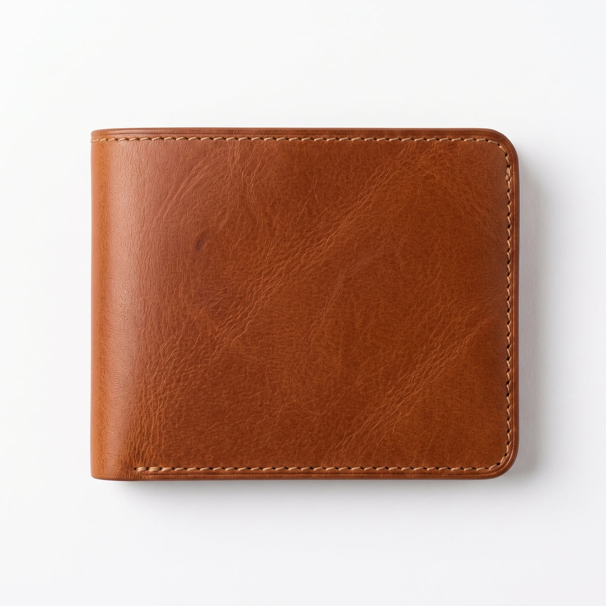 Flat lay front view of a tan brown leather bifold wallet resting on a plain white surface, showing rich natural leather grain with visible texture and tonal variation, contrasting cream stitching along all edges, and rounded corners, photographed directly from above with soft even lighting and a subtle shadow."