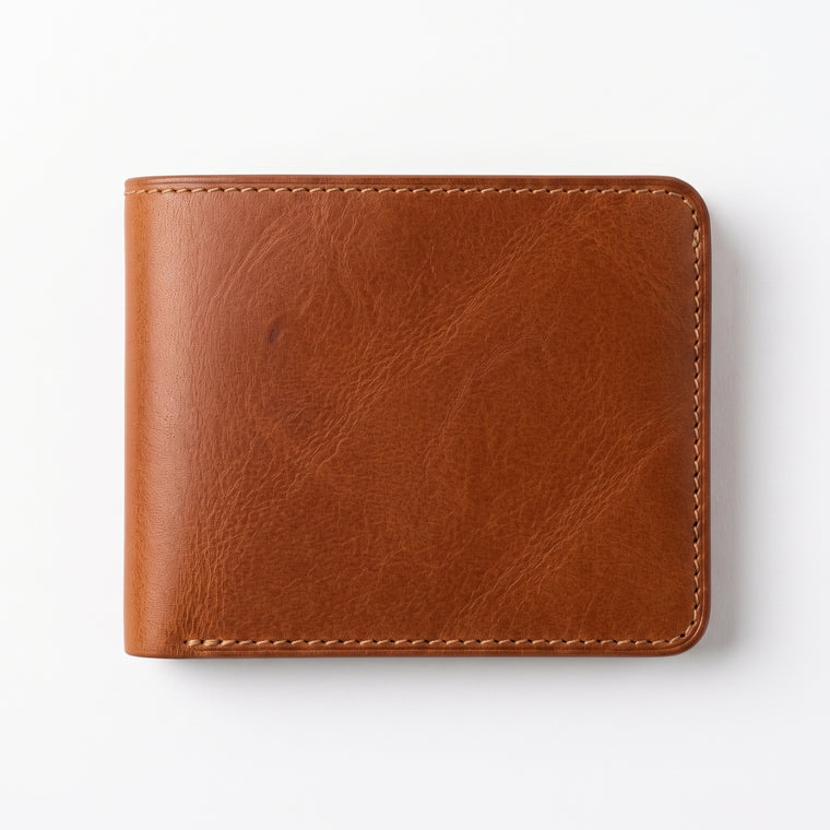 Flat lay front view of a tan brown leather bifold wallet resting on a plain white surface, showing rich natural leather grain with visible texture and tonal variation, contrasting cream stitching along all edges, and rounded corners, photographed directly from above with soft even lighting and a subtle shadow."