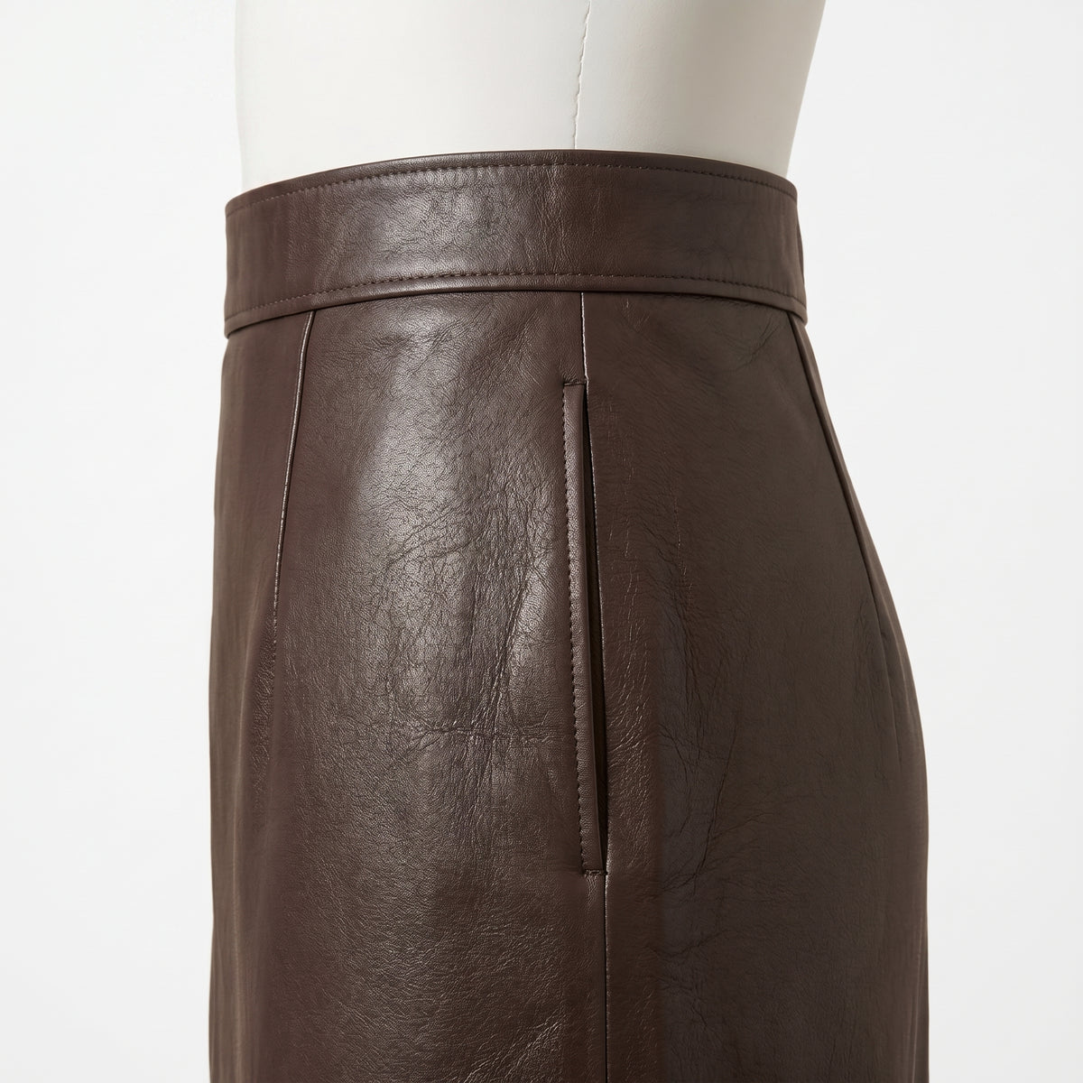 "Close-up of the waistband and a slit pocket on a dark brown leather pencil skirt, showing the stitching and leather grain texture."