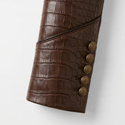 "Close-up detail of a brown crocodile-embossed leather coat's cuff with five gold crest buttons."