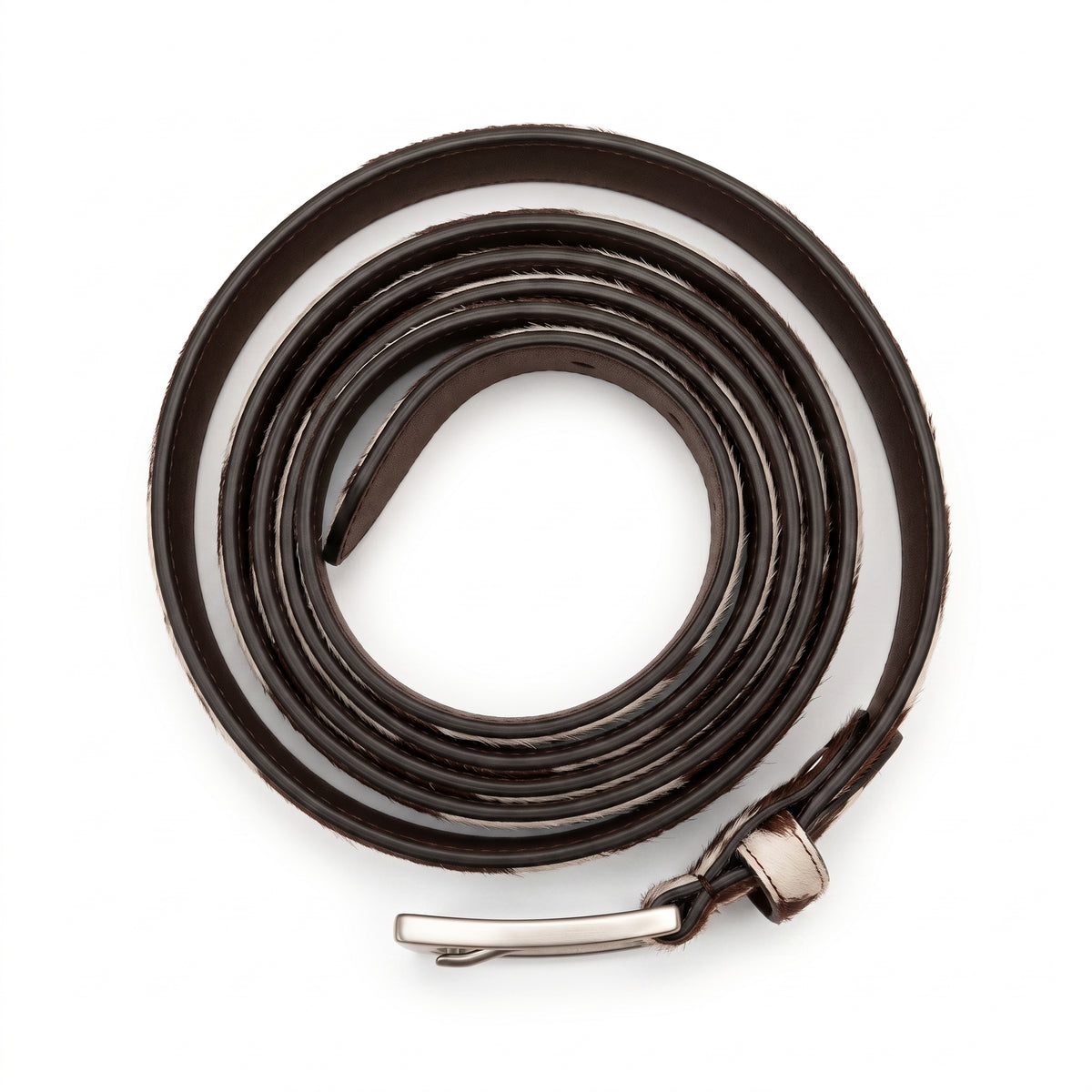 "Overhead view of a thin brown and white cow-print leather belt tightly coiled into a spiral, with a silver-tone buckle at the bottom, photographed on a white background."