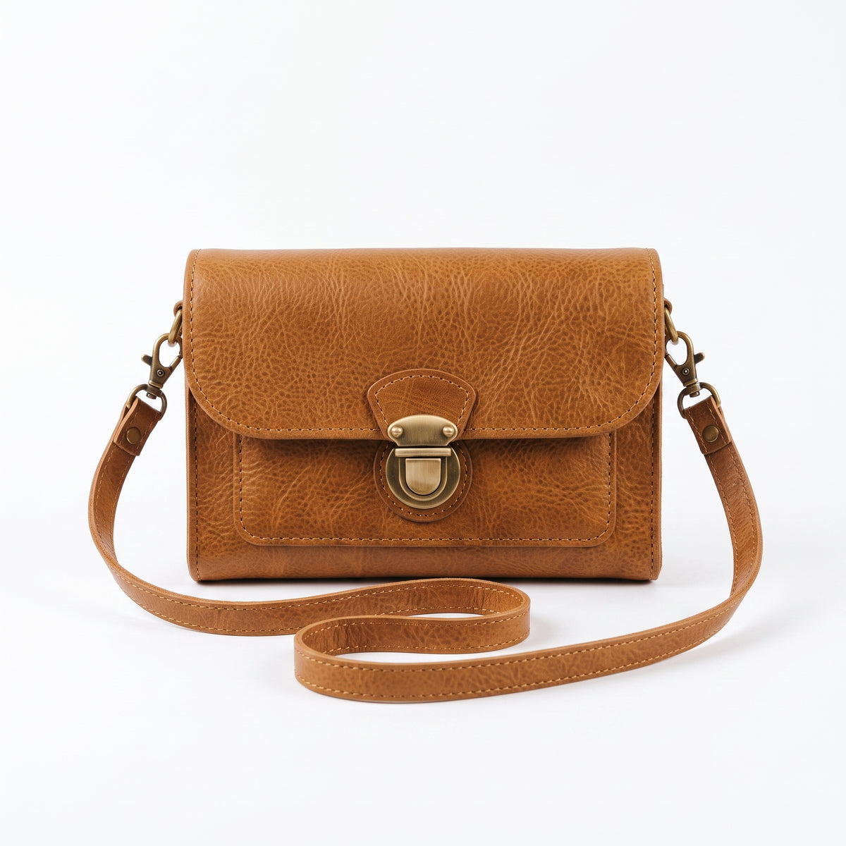 "Front view of a tan leather crossbody bag with a vintage brass push-lock clasp on the flap, and an adjustable strap looped loosely in front against a light background."