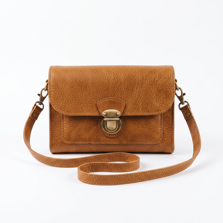 "Front view of a tan leather crossbody bag with a vintage brass push-lock clasp on the flap, and an adjustable strap looped loosely in front against a light background."