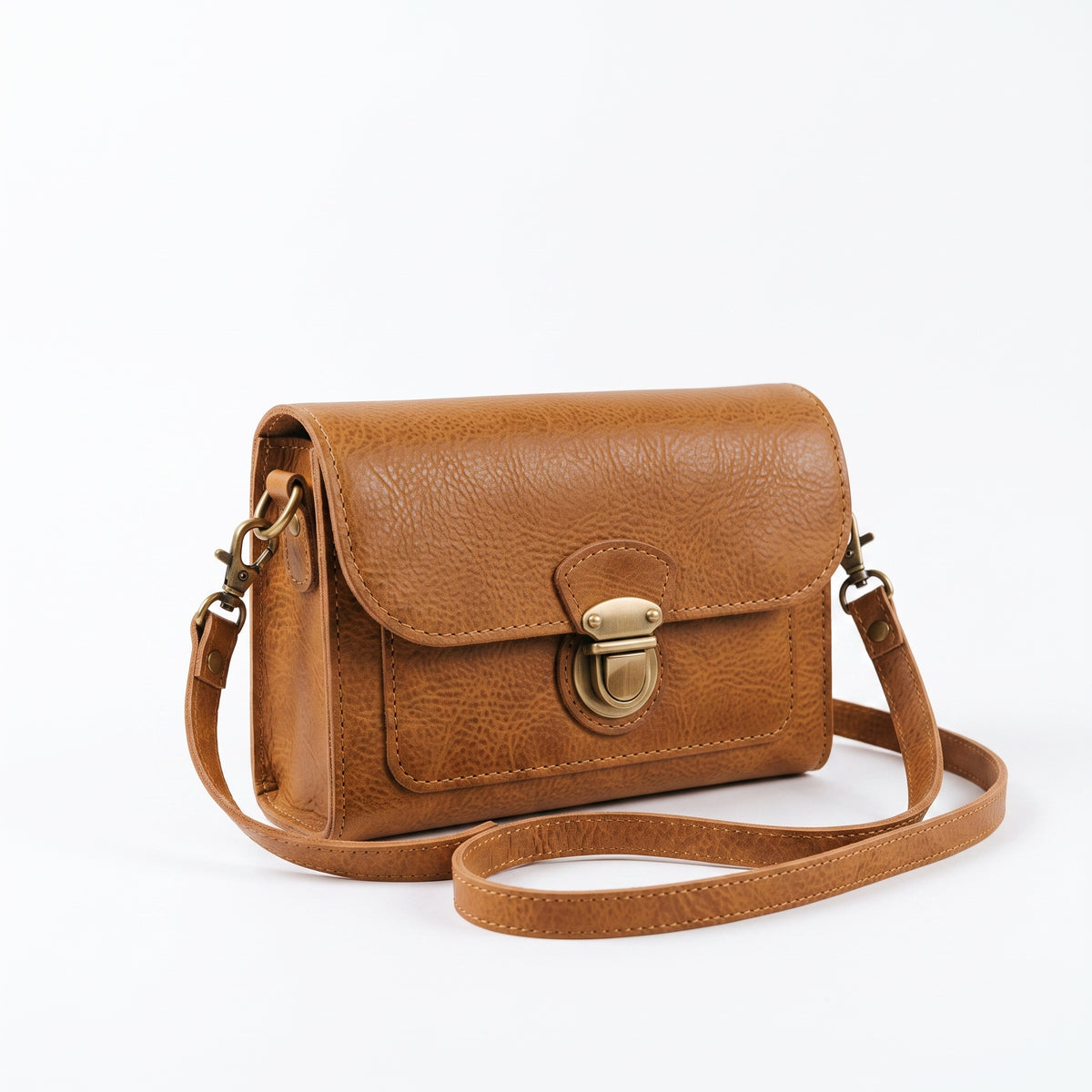 "Angled three-quarter view of a tan leather crossbody bag showing the brass push-lock clasp, adjustable strap with swivel hooks, and leather grain texture against a light background."