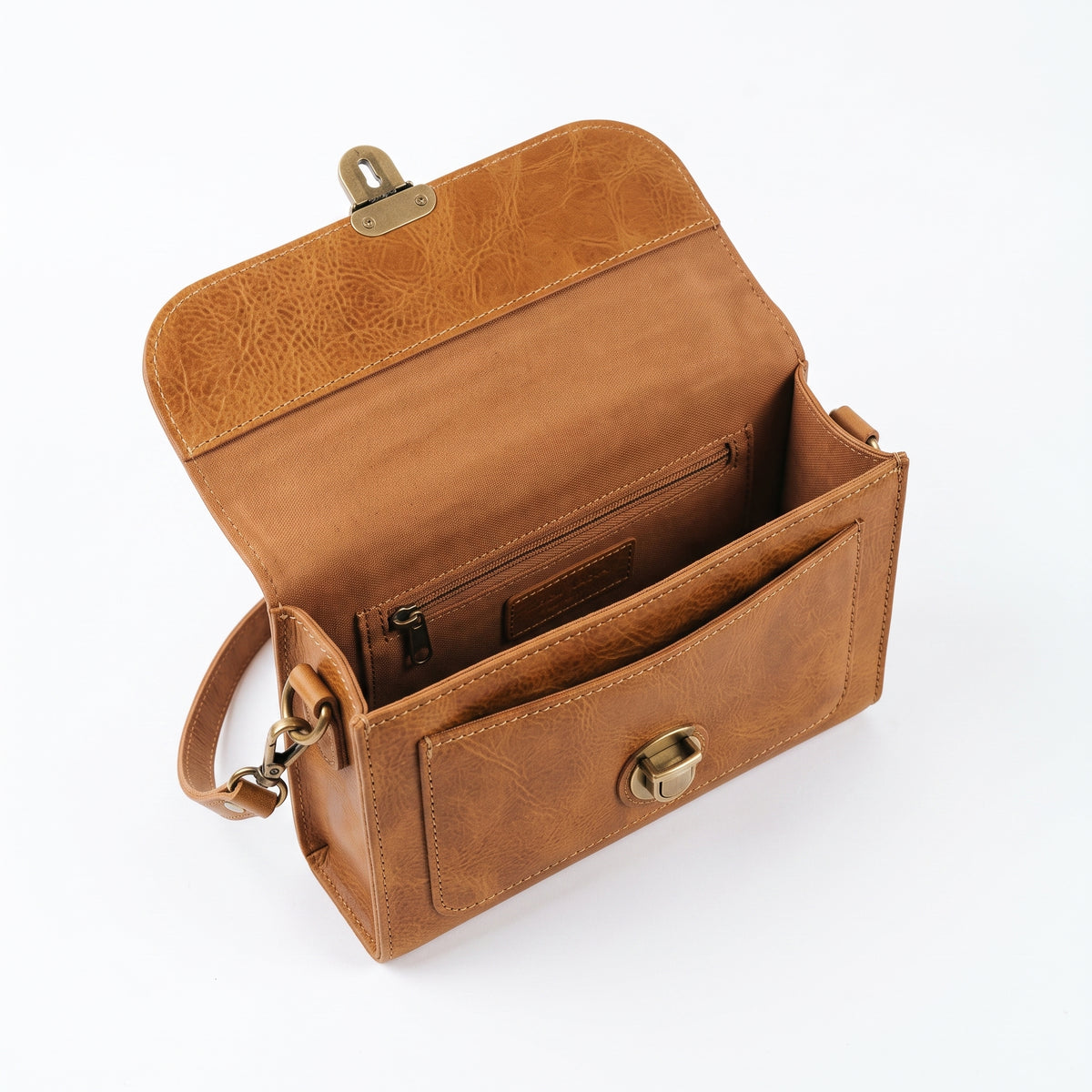 "Top view inside an open tan leather crossbody bag showing fabric lining, a zippered pocket, a slip pocket, and the brass lock mechanism on the flap."