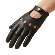 "A hand wearing a black leather driving glove with four circular ventilation holes on the knuckle area, perforated fingers, and a snap-button wrist strap, photographed on a white background."