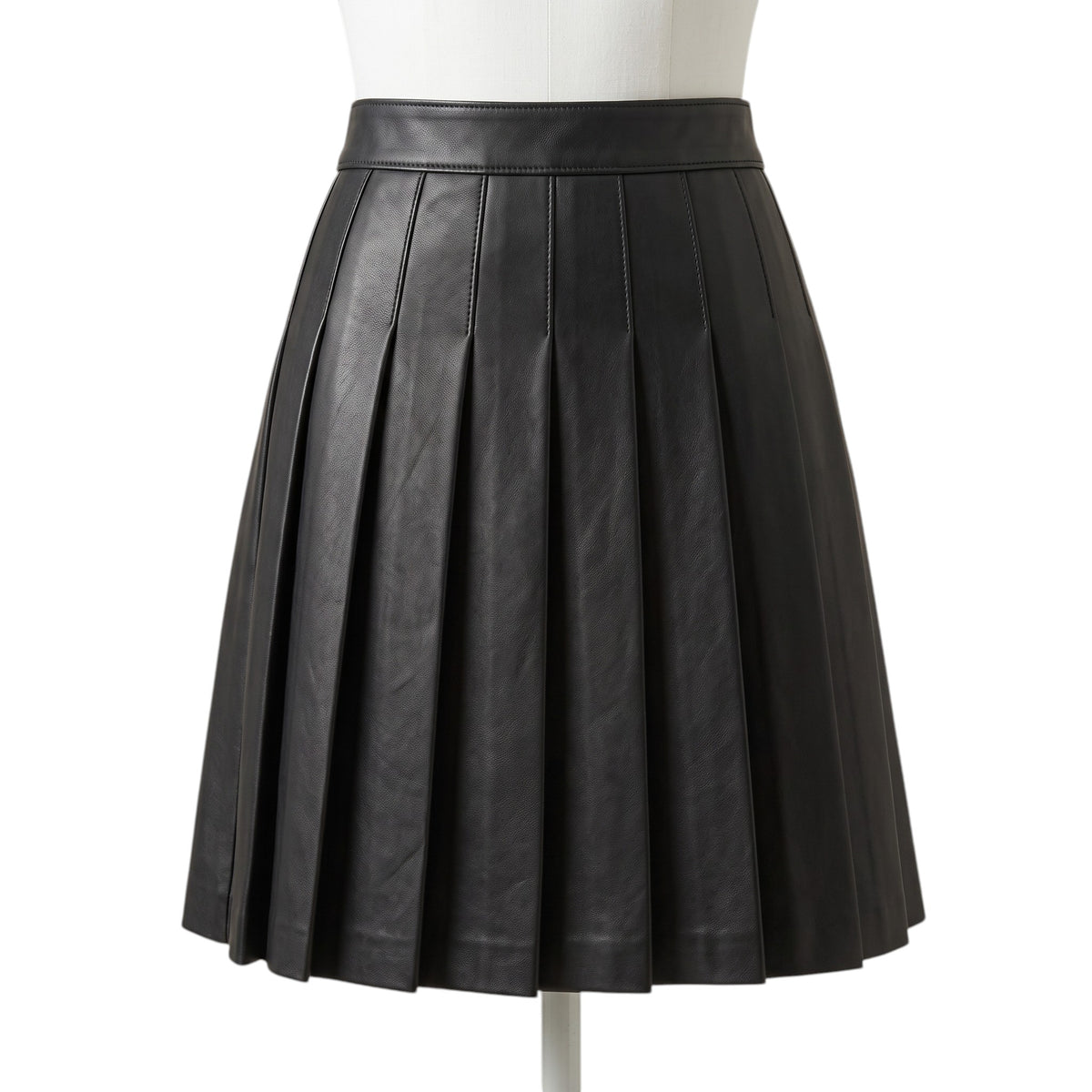 "A black leather pleated mini skirt on a mannequin, showing a smooth waistband and full box pleats creating an A-line silhouette against a white background."