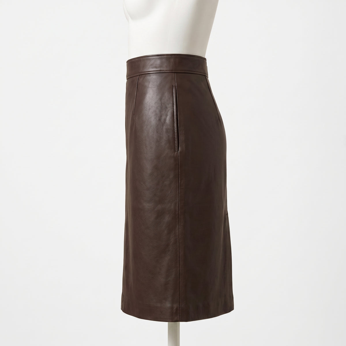 "Side profile view of the dark brown leather pencil skirt on a mannequin, showing the waistband, front seam, and clean silhouette against a light background."