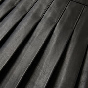 "Extreme close-up of the pleats on a black leather skirt, shot at an angle showing the leather grain texture and stitched pleat lines."