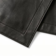 "Extreme close-up of the hem edge on a black leather skirt, showing the leather grain texture and edge stitching against a white background."