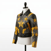 "Angled view of a black leather biker jacket with yellow and gray star graphic panels, asymmetric front zipper, zip pockets, and belted waist, displayed on a mannequin against a white background."