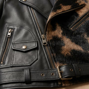 "Close-up detail of a black leather biker jacket showing zip pocket, snap-flap pocket, front zipper, buckle belt, and animal-print fur panel."